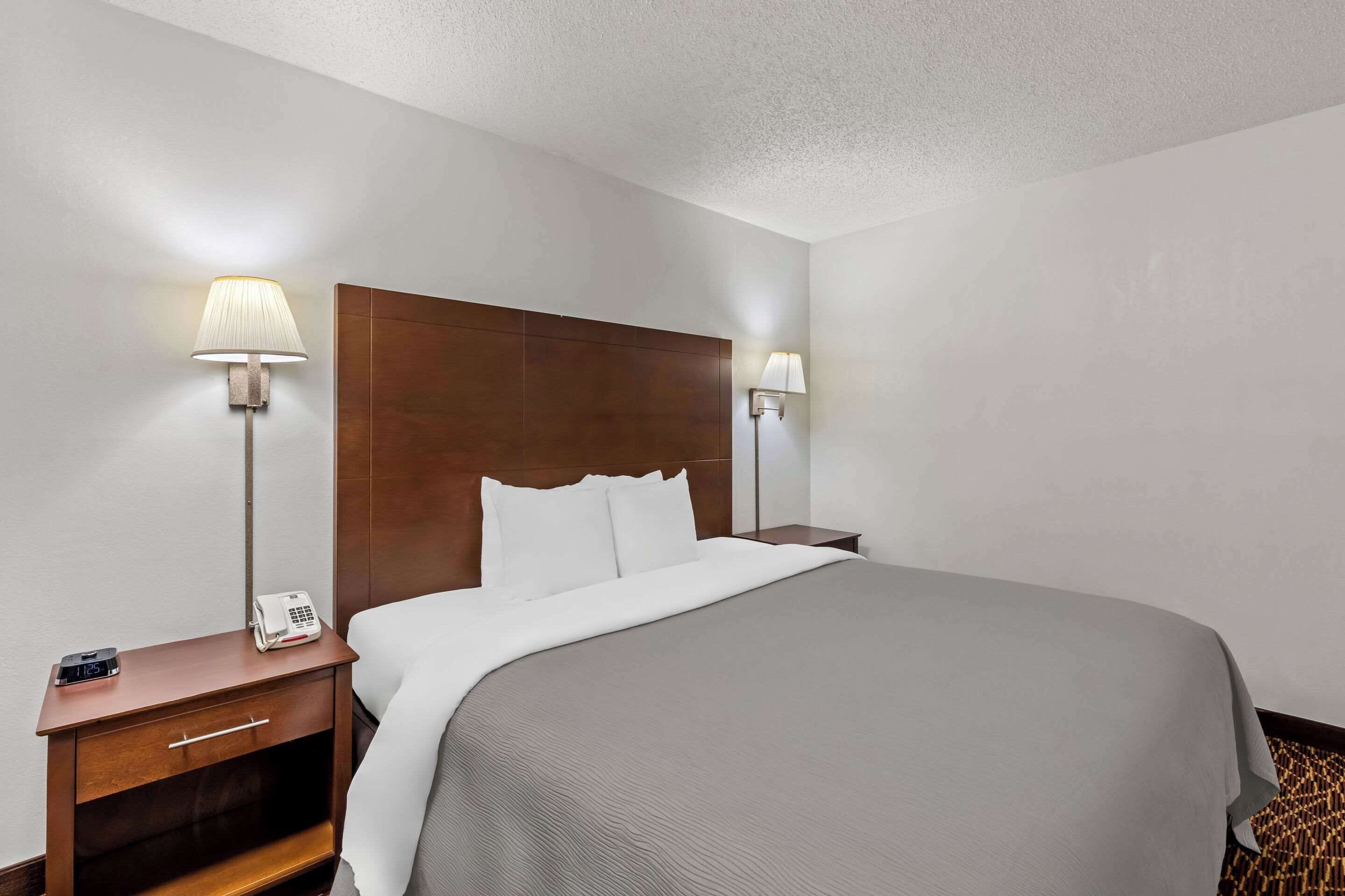 Une chambre d’hôtel avec un grand lit, deux tables de chevet avec des lampes, une petite table de nuit avec un téléphone et une horloge fixée au mur.