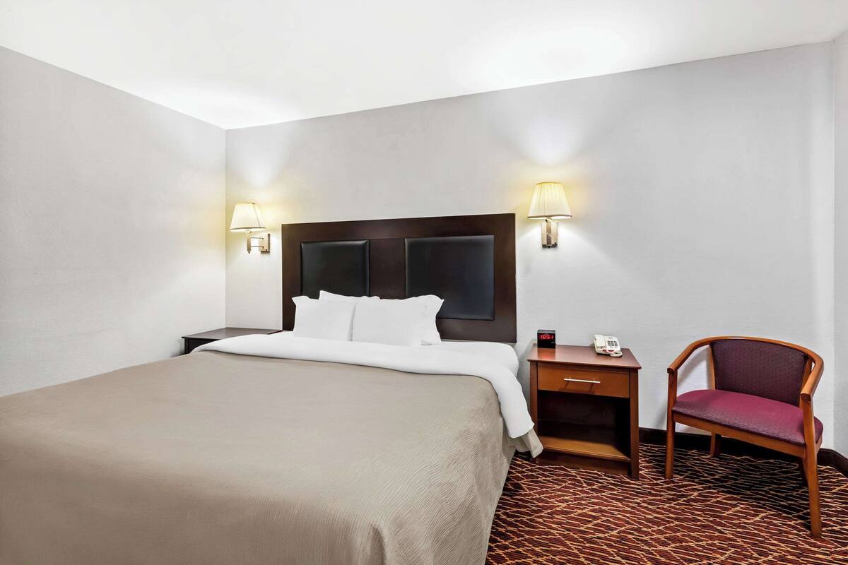 Une chambre d’hôtel avec un grand lit, deux tables de chevet, une chaise et deux lampes fixées au mur.