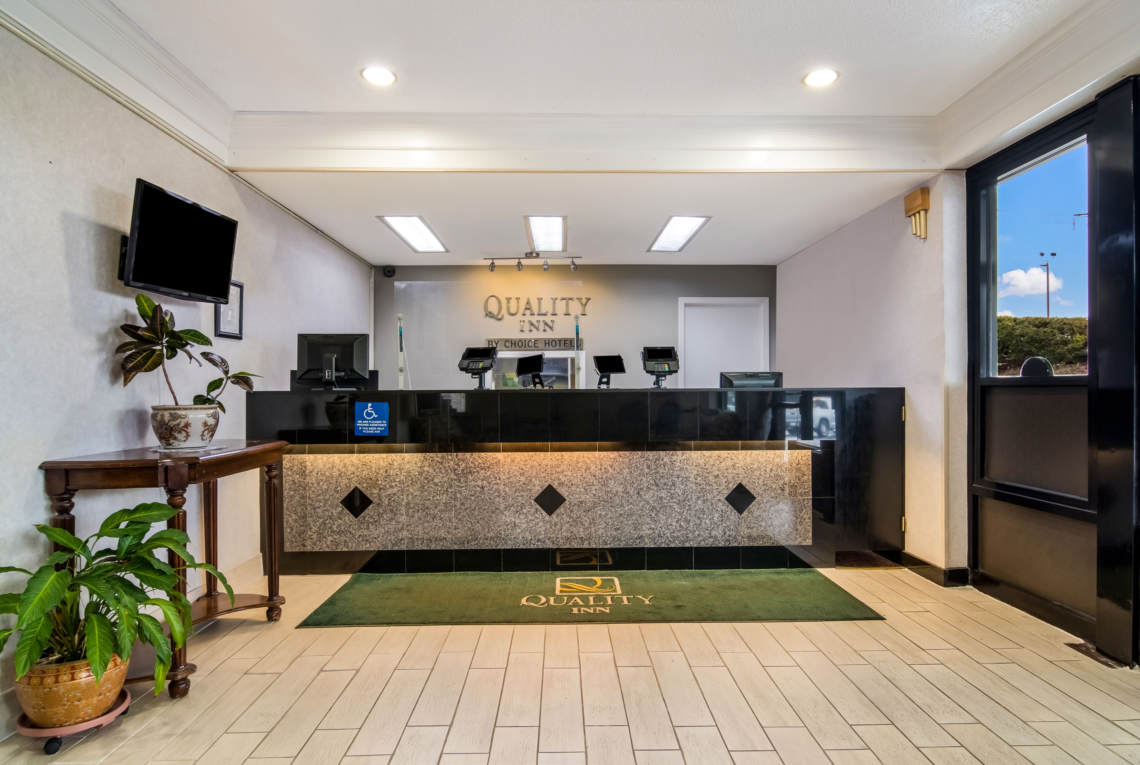 Uma área de recepção com balcão, televisão de tela plana e uma placa com a inscrição 'Quality Inn By Choice Hotel'.
