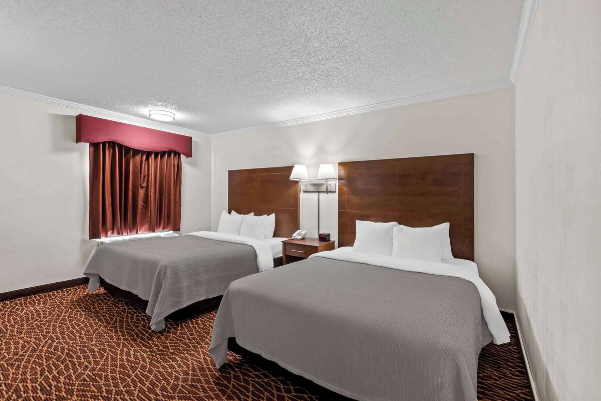 Une chambre d’hôtel avec deux lits, une tête de lit en bois, une table de chevet, un téléphone et une moquette à motifs.