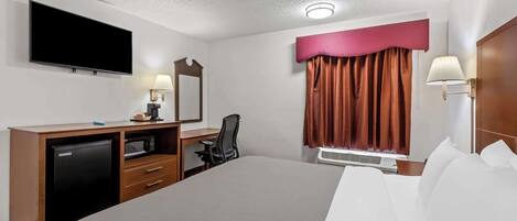 Una habitación de hotel con una cama grande, un escritorio con computadora, televisor, microondas y una ventana con cortinas.