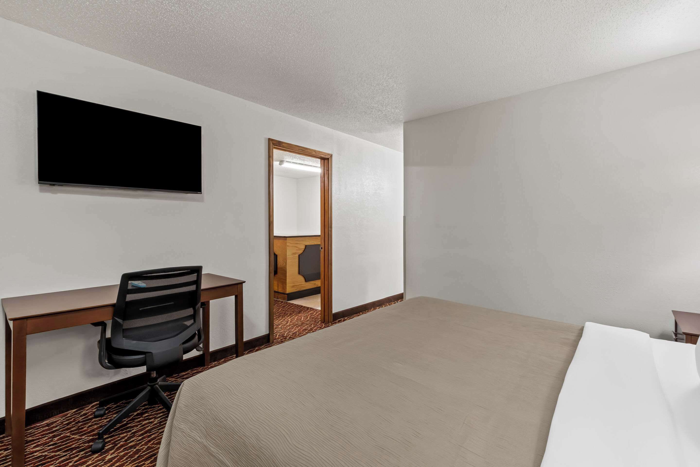 A hotel room with a bed, a desk with a chair, a television, and a door leading to a bathroom.