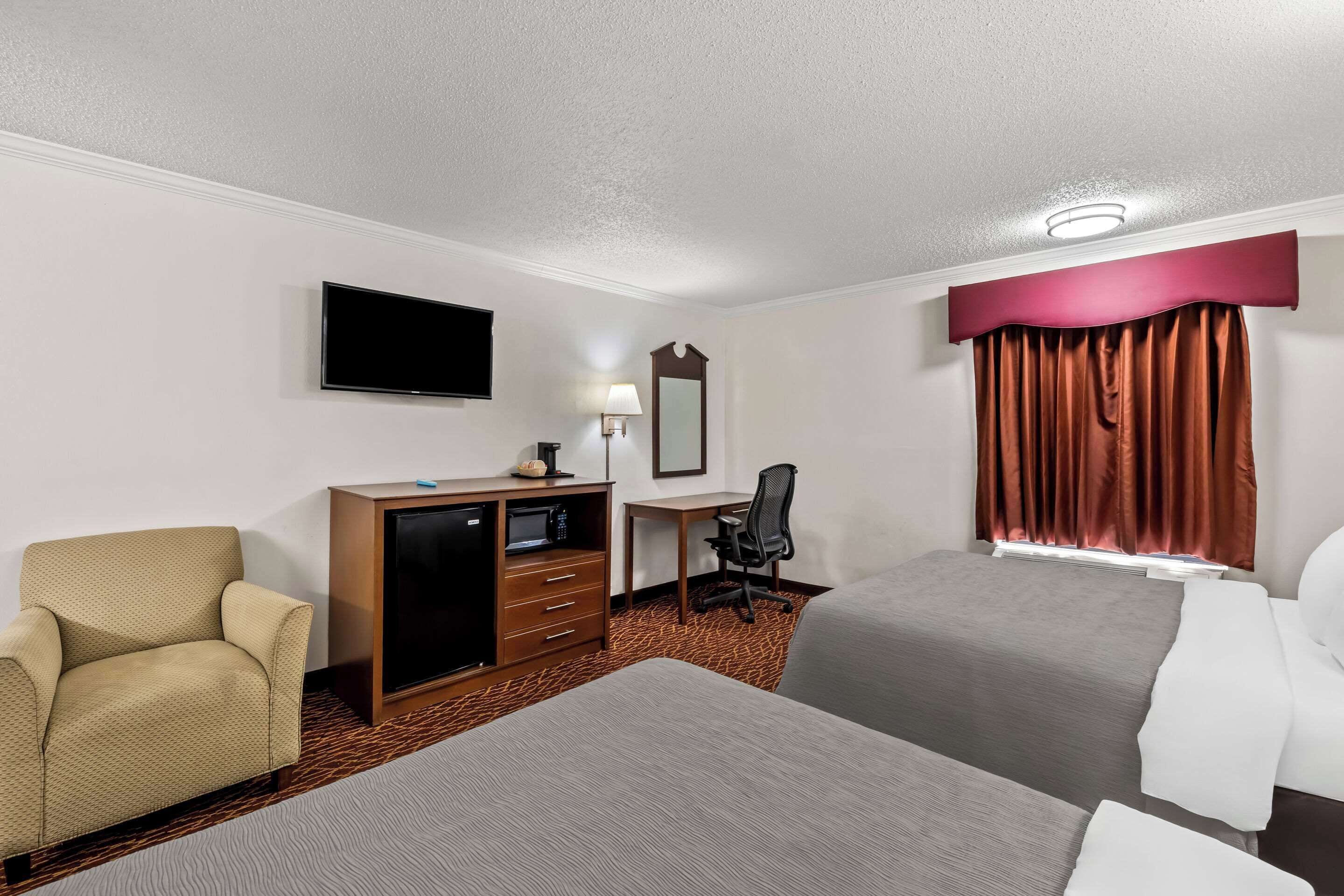 A hotel room with two beds, a desk, a chair, a TV, and a mirror.