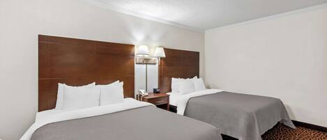 A hotel room with two beds, a wooden headboard, a nightstand with a lamp, and a patterned carpet.