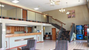 A spacious lobby with a high ceiling, a staircase, a bar area, and striped armchairs.
