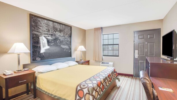 A hotel room with a large bed, two bedside tables with lamps, a TV, a desk, and a window with curtains.