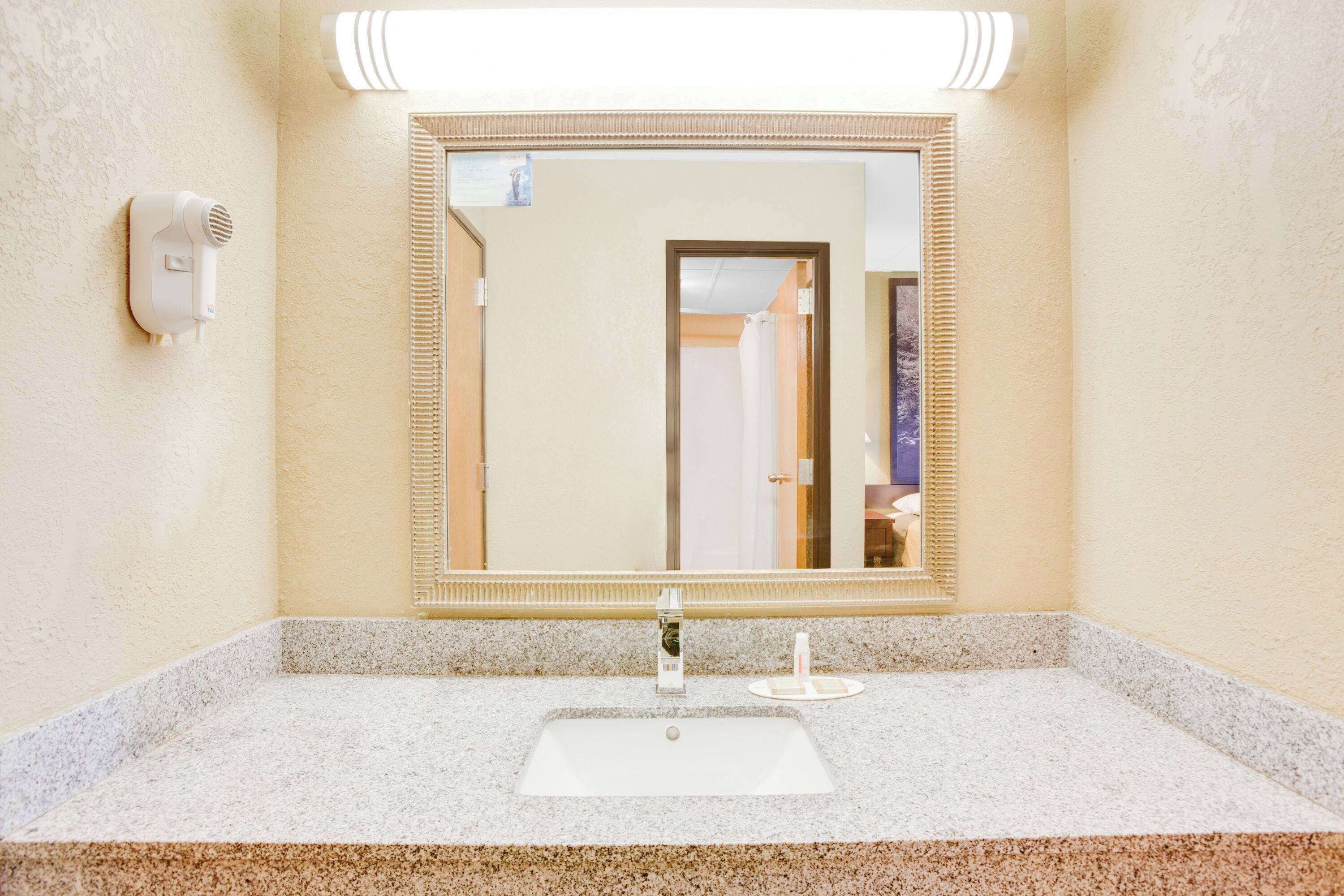 Un baño con lavabo, espejo y secador de pelo montado en la pared.