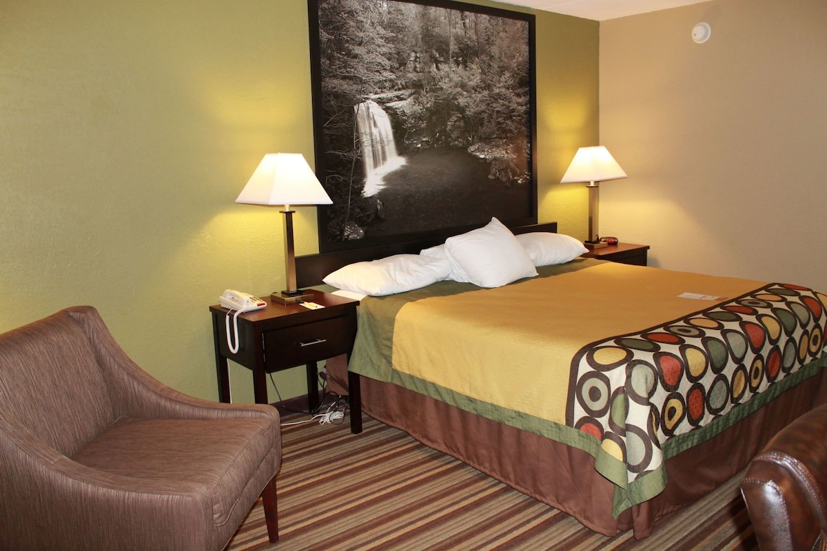A hotel room with a bed, two bedside lamps, a chair, a telephone, and a painting of a waterfall.
