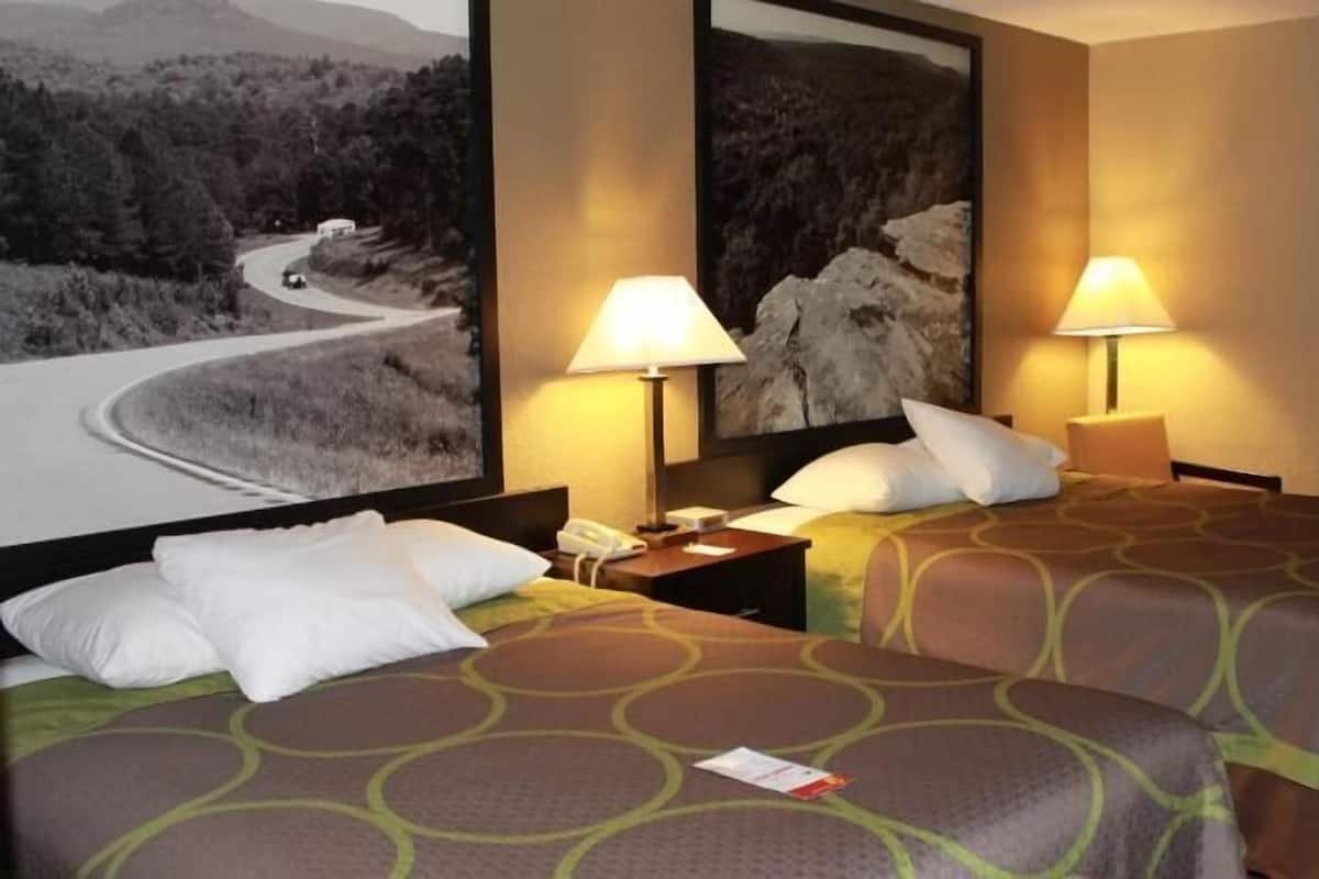 A hotel room with two beds, a nightstand, a lamp, and a large framed picture on the wall.