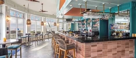 A bar area with a long counter, bar stools, and a variety of bottles and glasses.