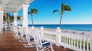 A beachside terrace with white rocking chairs and a white balustrade overlooking the ocean.