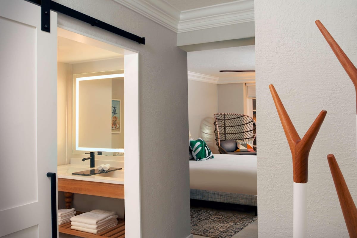 Habitación de hotel con baño, una cama, una silla y una pared decorada con madera.
