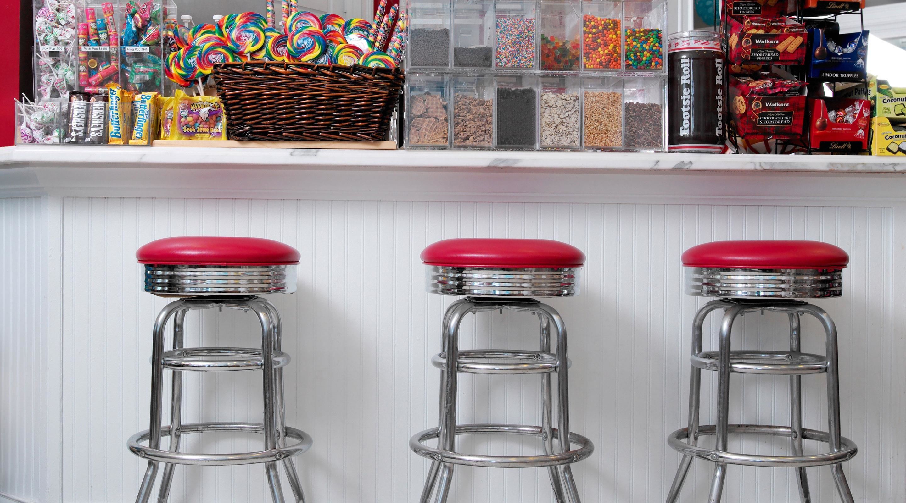 Un área de bar con tres taburetes y una estantería llena de golosinas y refrigerios.