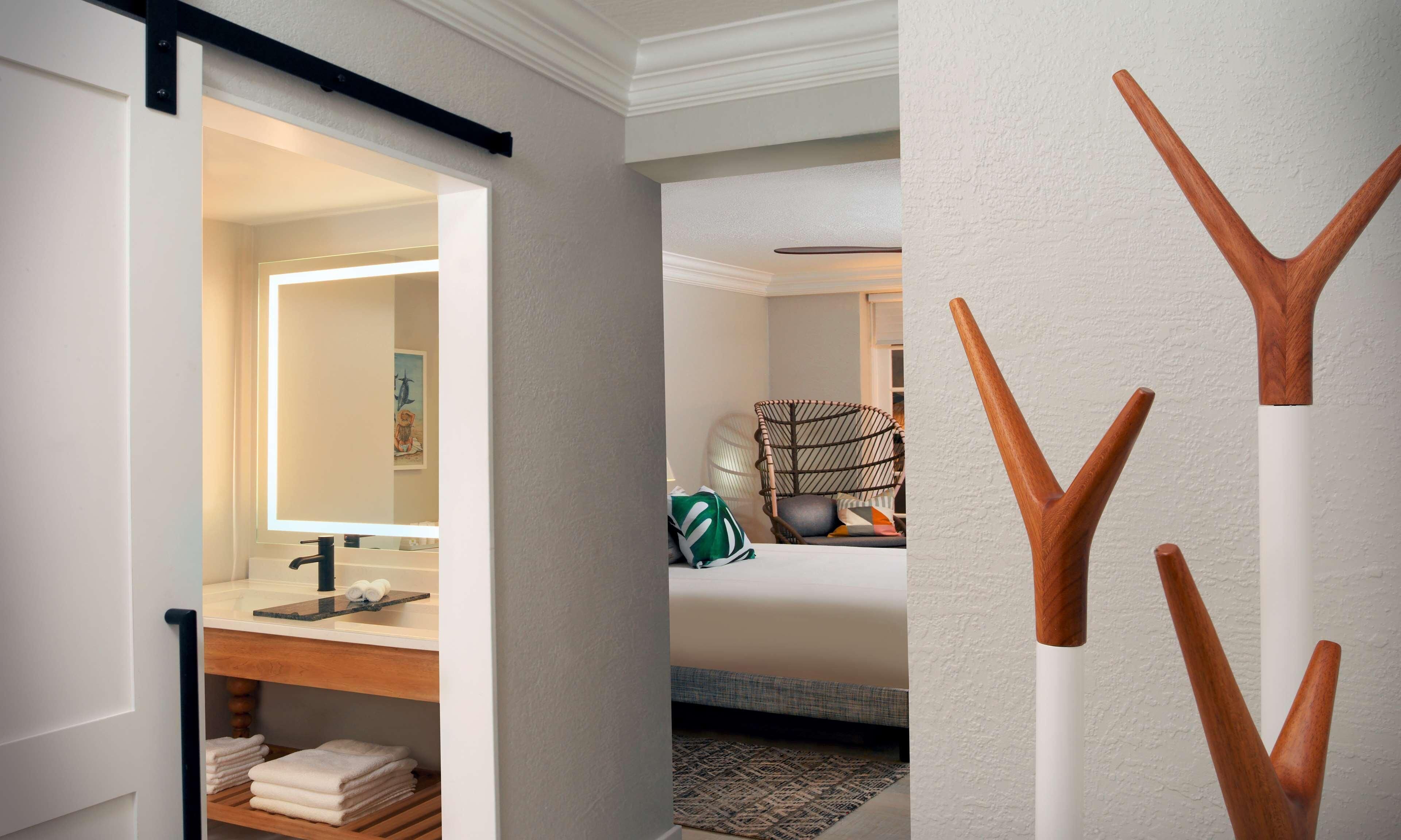Habitación de hotel con baño, una cama, una silla y una pared decorada con madera.