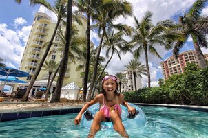 Zona de piscina con palmeras y un edificio al fondo.