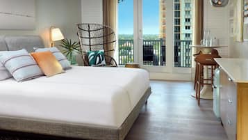 A hotel room with a bed, a chair, a desk, and a view of a building through the window.