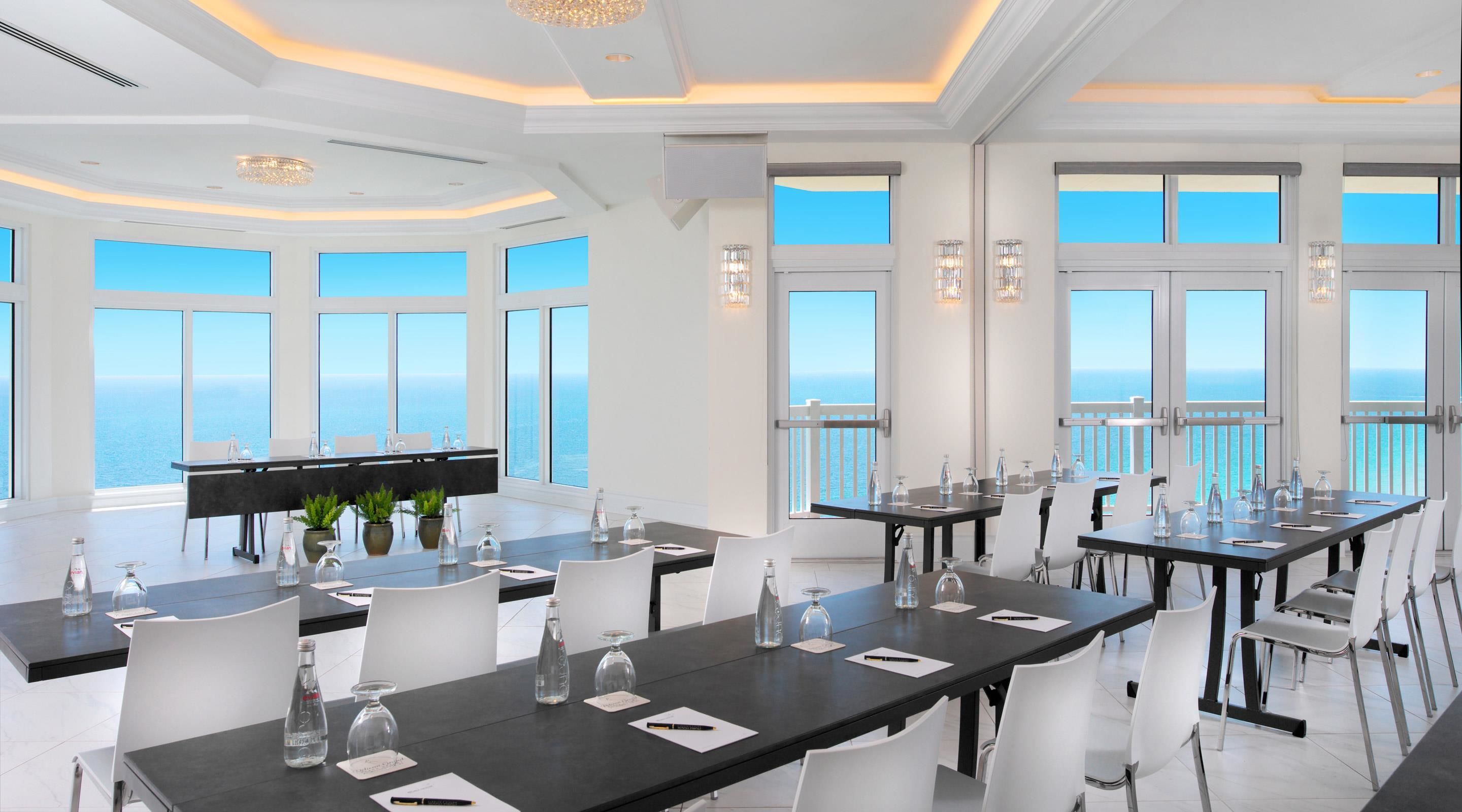 Ein geräumiger Essbereich mit großen Fenstern und Meerblick, eleganten Kronleuchtern und modernen Tischdekorationen.