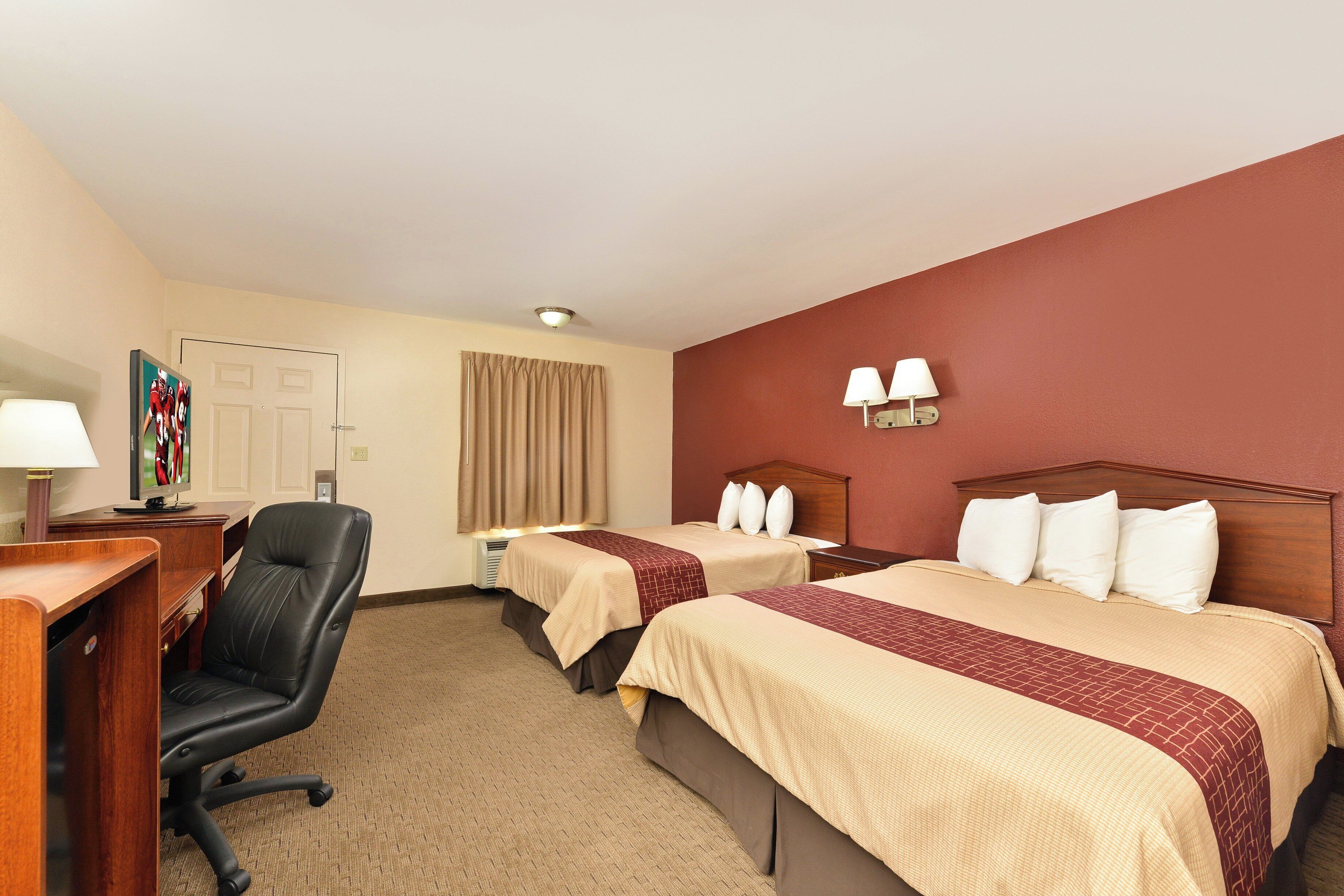 Une chambre d’hôtel avec deux lits, un bureau, une chaise, une télévision et une fenêtre avec des rideaux.