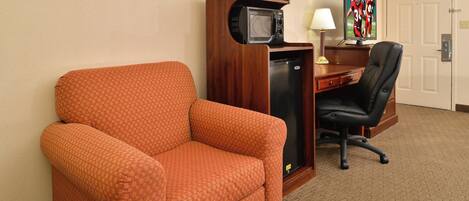 Una habitación de hotel con un sillón naranja, un escritorio con computadora y televisor, y una puerta.