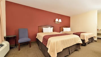 Ein Hotelzimmer mit zwei Betten, einem Sessel, einem Tisch und einer Wandlampe.