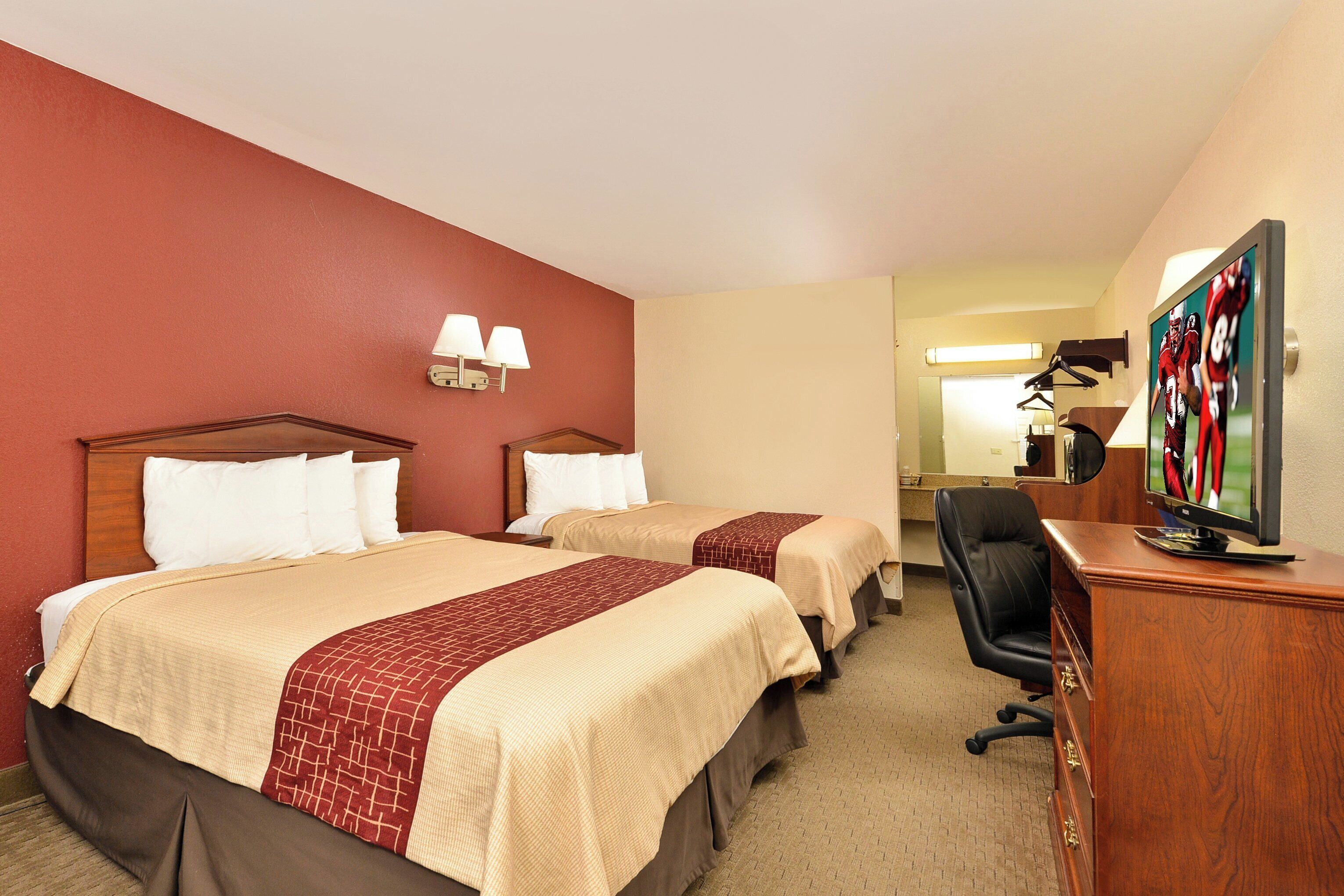 A hotel room with two beds, a desk with a television, and a mirror.