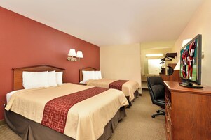 A hotel room with two beds, a desk with a television, and a mirror.