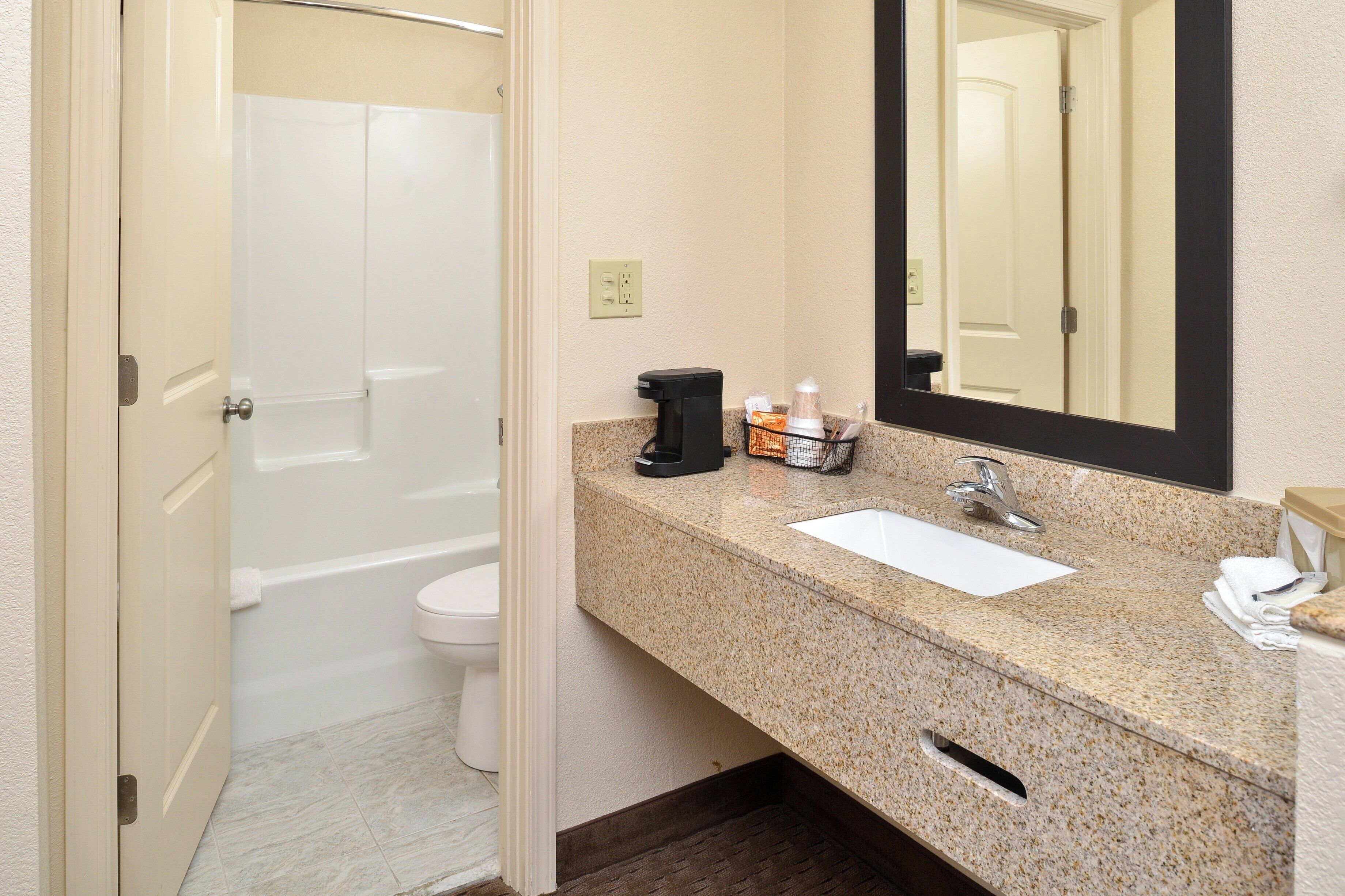 Une salle de bain avec des toilettes blanches, un lavabo, un miroir et un espace douche.