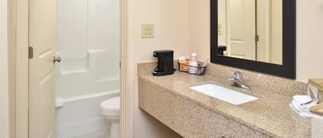 Un baño con inodoro blanco, lavamanos, espejo y zona de ducha.