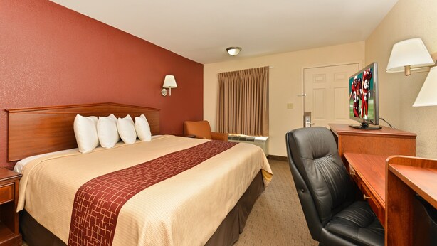 A hotel room with a large bed, a desk, a chair, a TV, and a lamp. - Red Roof Inn Dalton (Dalton)
