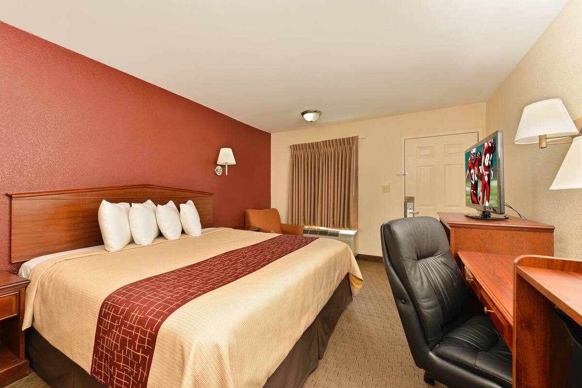 A hotel room with a large bed, a desk, a chair, a TV, and a lamp.