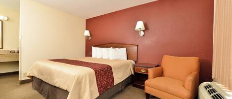 A hotel room with a bed, a chair, a nightstand, a lamp, and a heater.