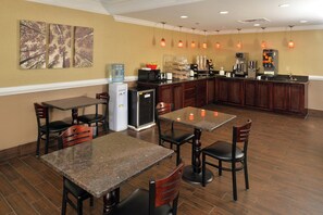 Un comedor de hotel con mesas, sillas, dispensador de agua, refrigerador y estación de café.