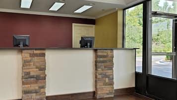 Une salle d’attente avec un comptoir en pierre, une porte portant l’inscription « Bureau » et une fenêtre donnant sur un espace verdoyant.