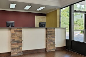 A reception area with a stone counter, a door labeled 'Office,' and a window with a view of greenery. - Red Roof Inn Dalton (Dalton)