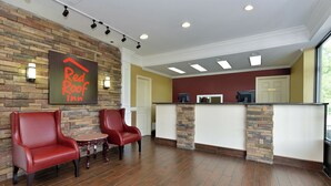 A Red Roof Inn reception area with a stone wall, two red leather chairs, a small table, and a reception desk with a computer. - Red Roof Inn Dalton (Dalton)