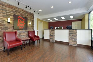 A Red Roof Inn reception area with a stone wall, two red leather chairs, a small table, and a reception desk with a computer. - Red Roof Inn Dalton (Dalton)
