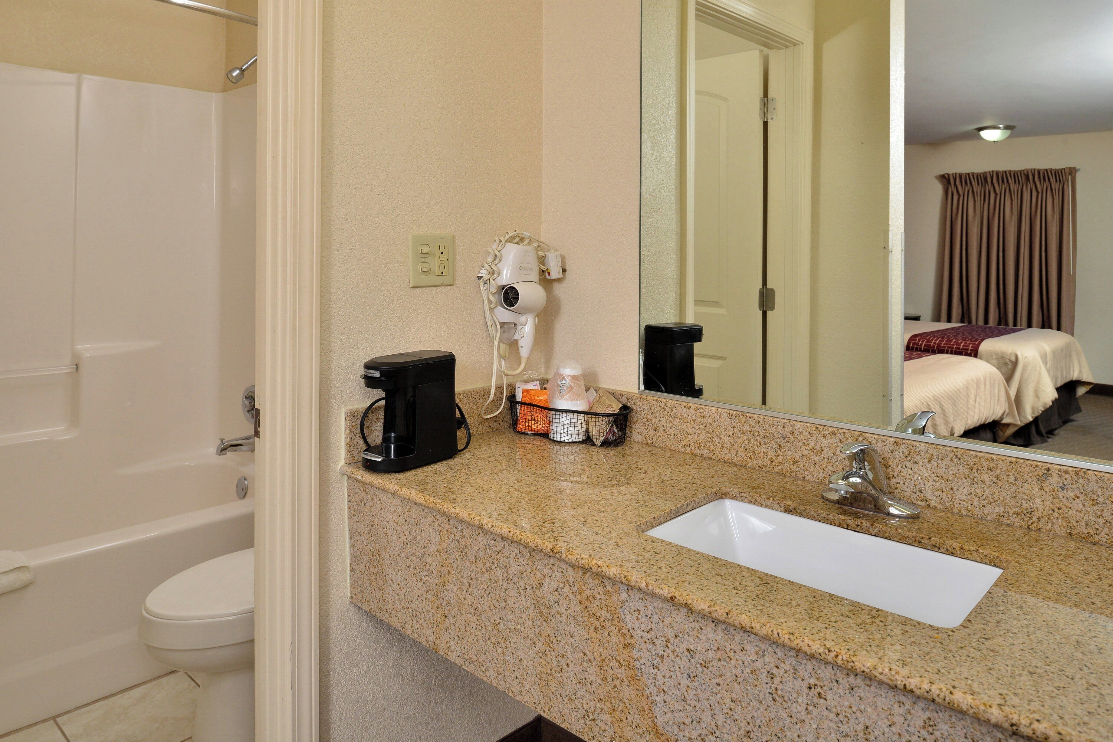 A bathroom with a sink, a hairdryer, a coffee maker, and a mirror.
