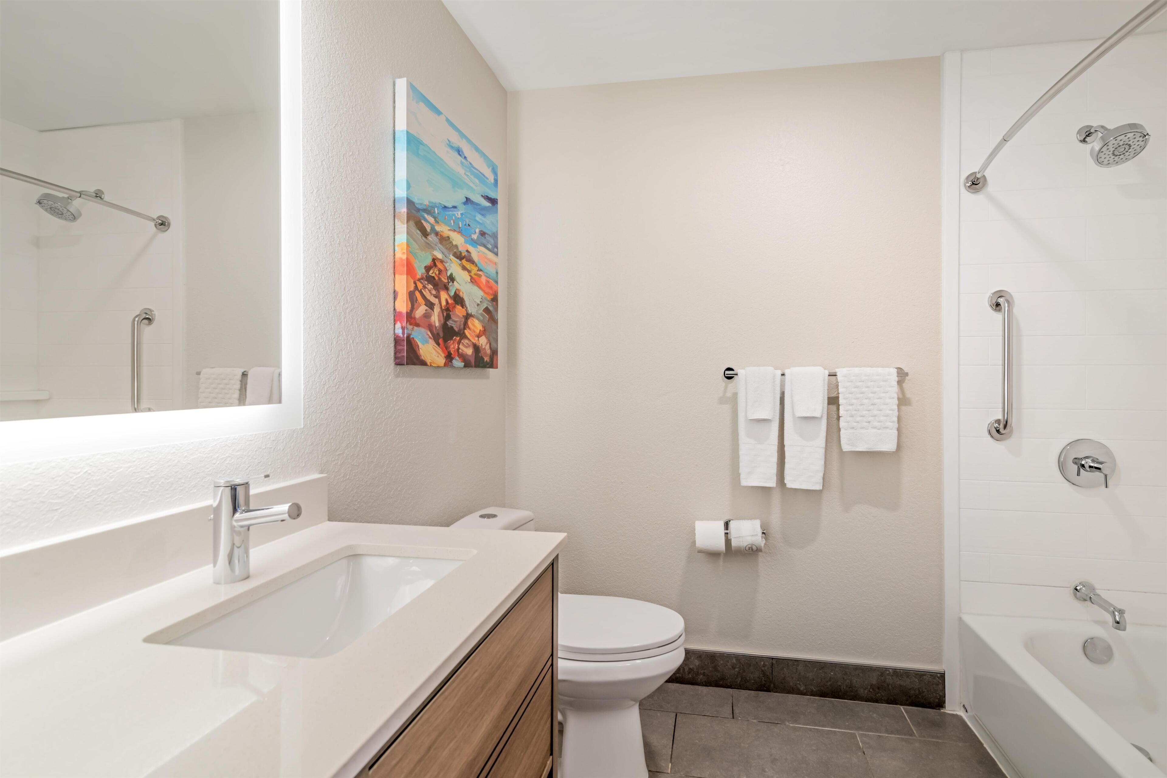A modern bathroom with a sink, toilet, shower, and a painting on the wall.