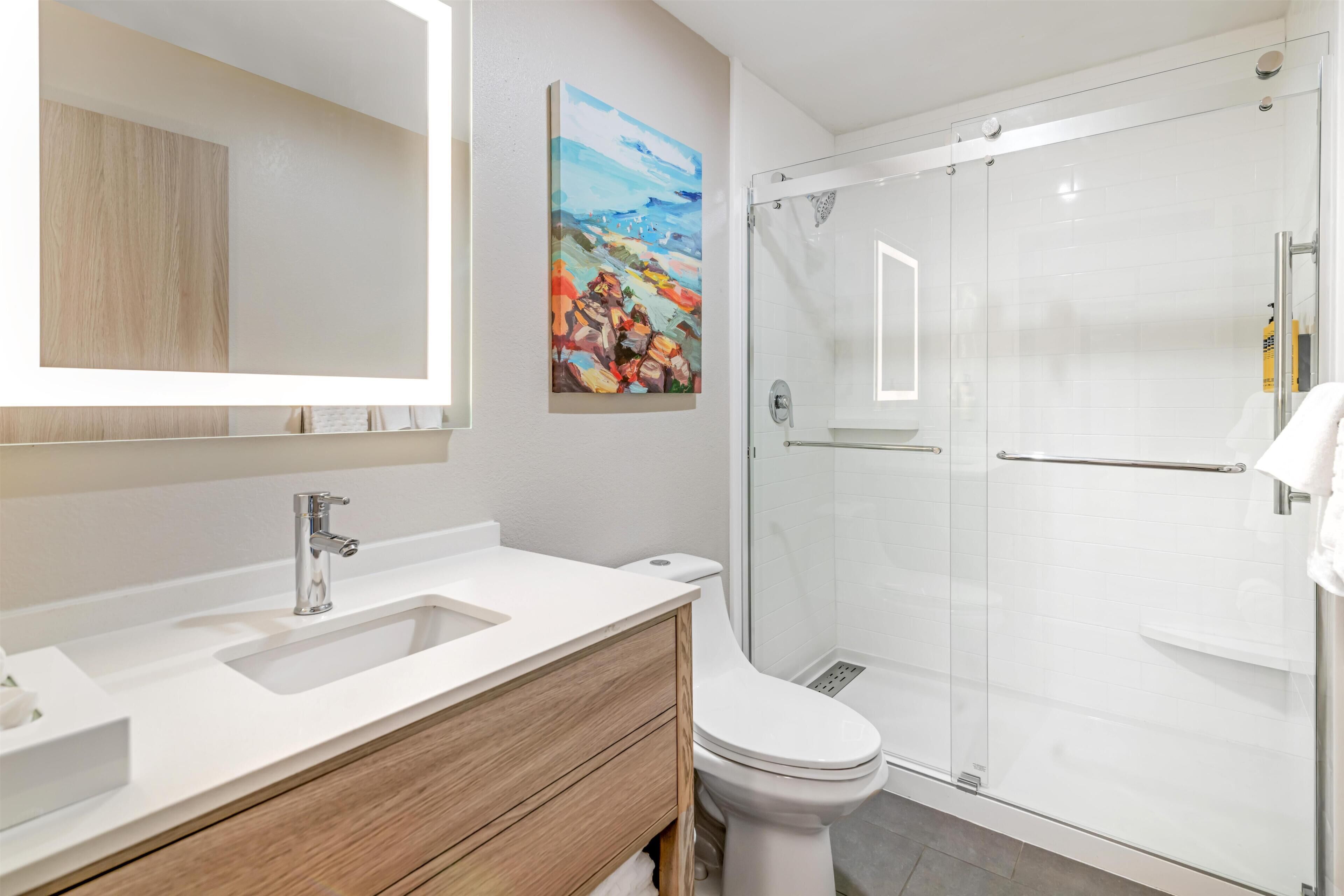 Ein modernes Badezimmer mit einem weißen Waschbecken, einem Holz-Waschtisch, einer Toilette und einer Duschkabine aus Glas.