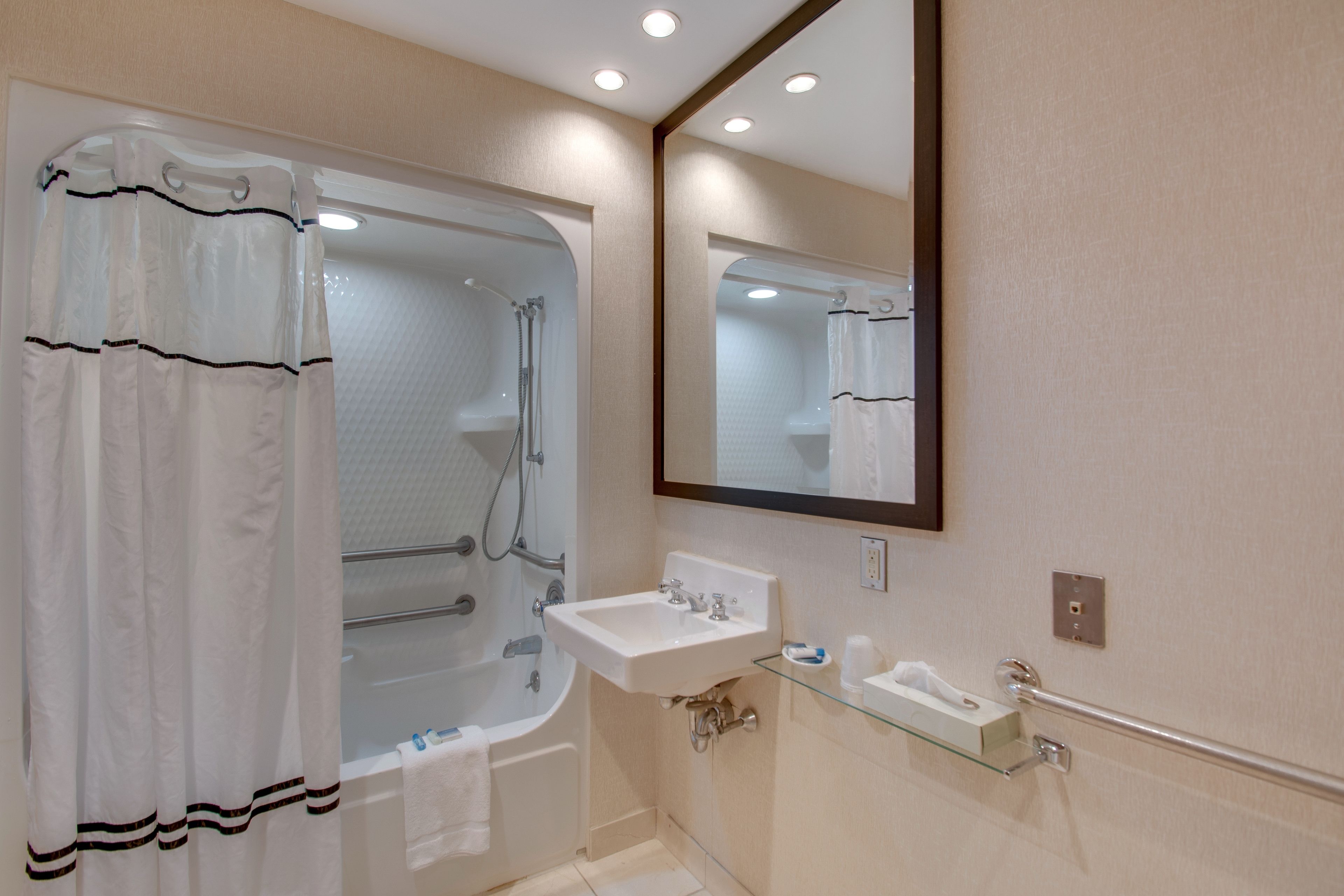 Un baño con bañera, lavabo, espejo y estante de vidrio.