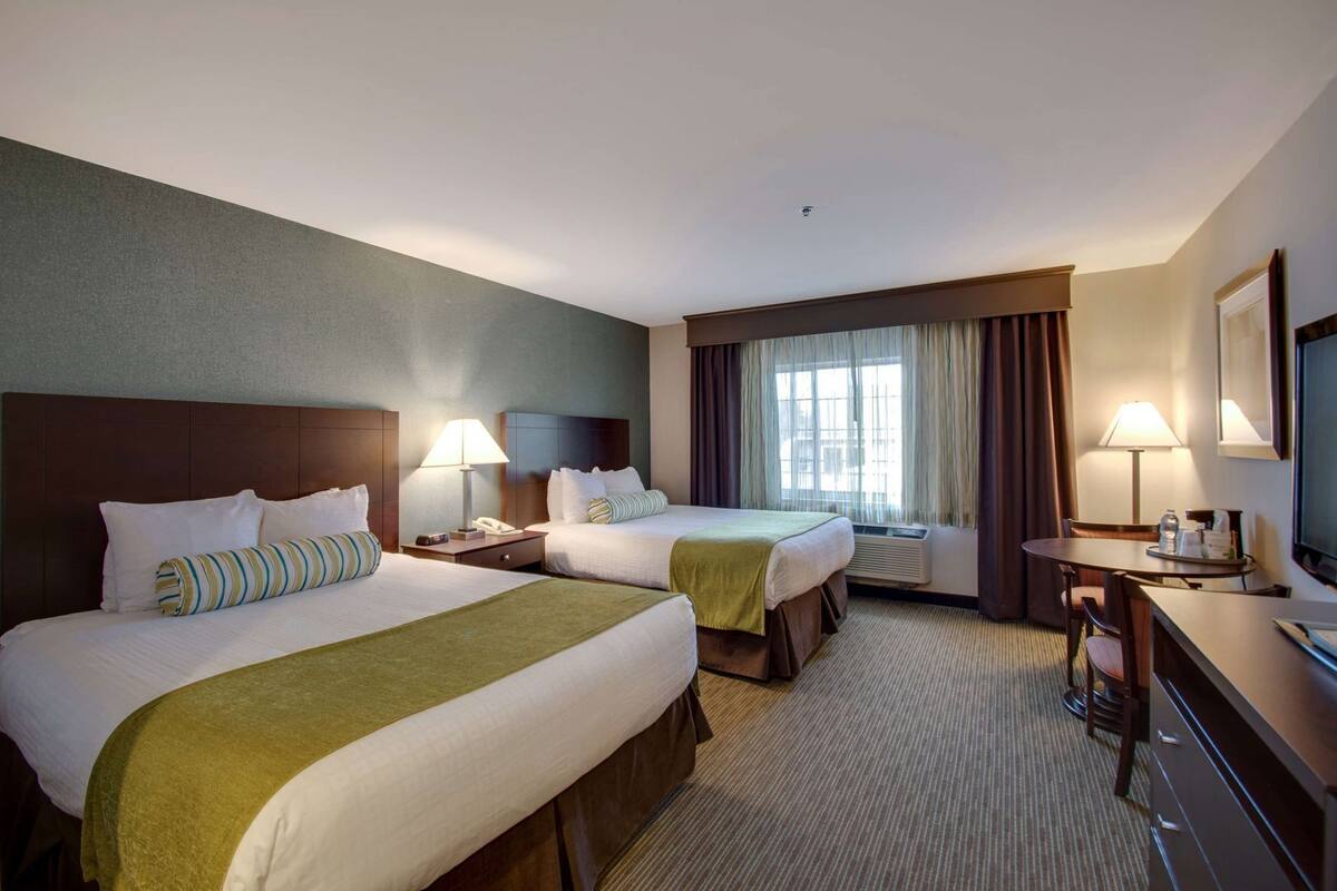 A hotel room with two beds, a desk, a chair, a television, and a window with curtains.