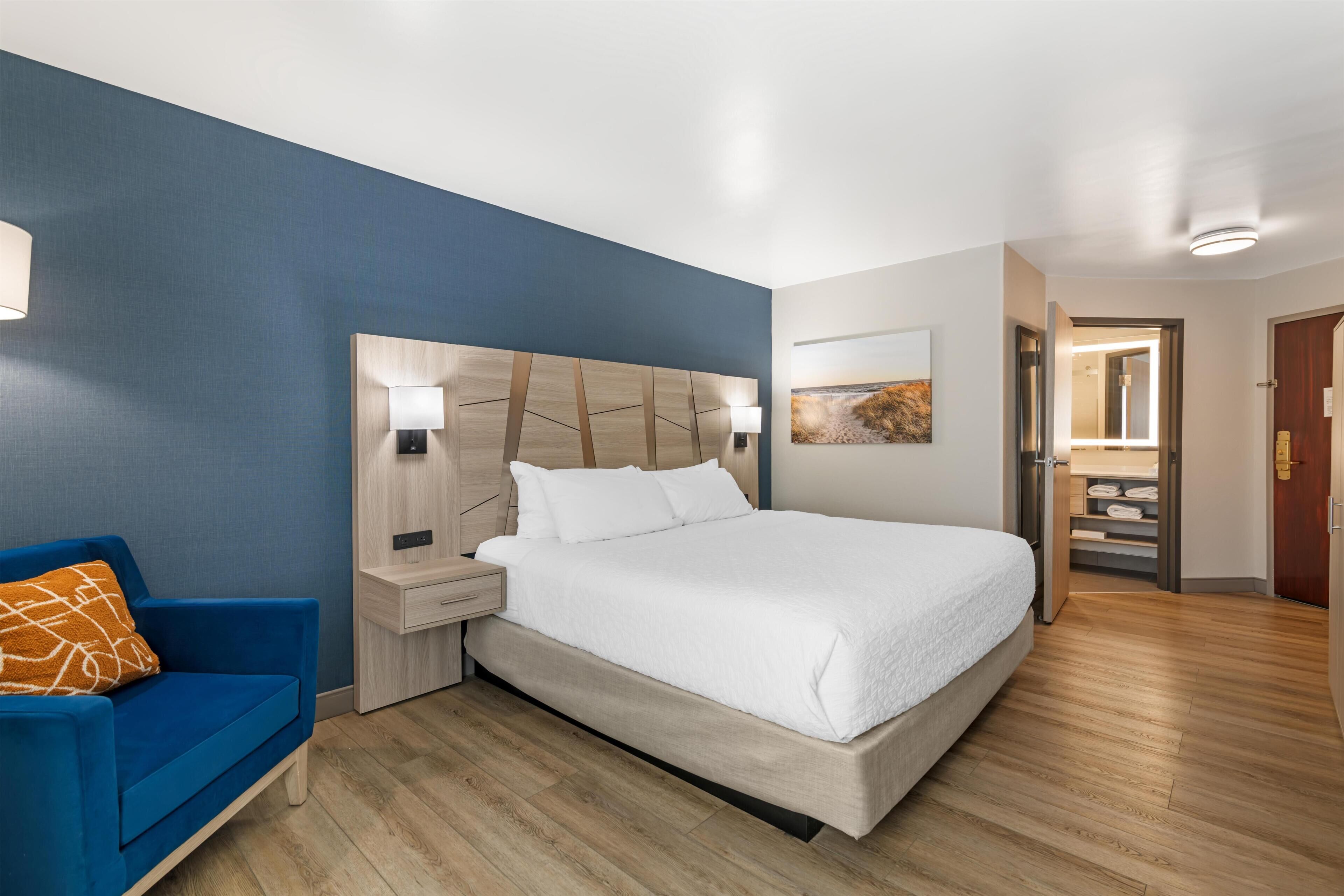 A hotel room with a bed, a nightstand, a blue sofa, and a wooden floor.