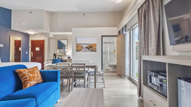 A modern living room with a blue sofa, a dining area, and a kitchen with a microwave. - Best Western Plus The Inn at Hampton (Hampton)