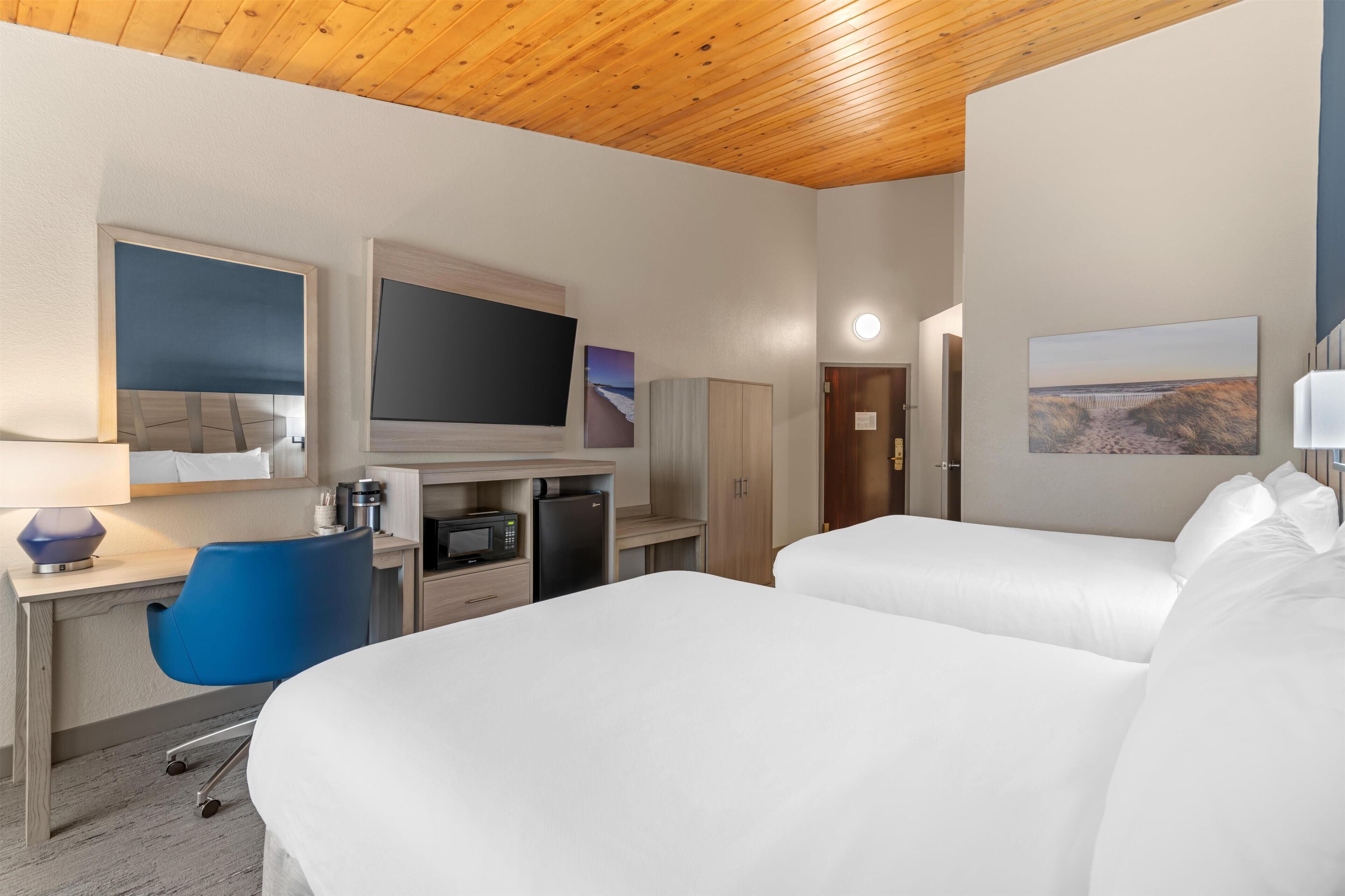 Habitación de hotel con dos camas, un escritorio con computadora, televisión, microondas y una silla azul.