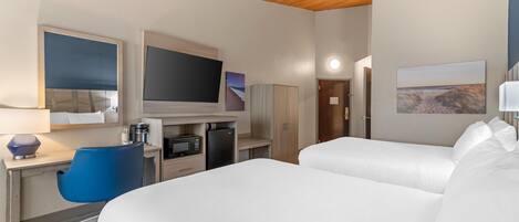 Habitación de hotel con dos camas, un escritorio con computadora, televisión, microondas y una silla azul.