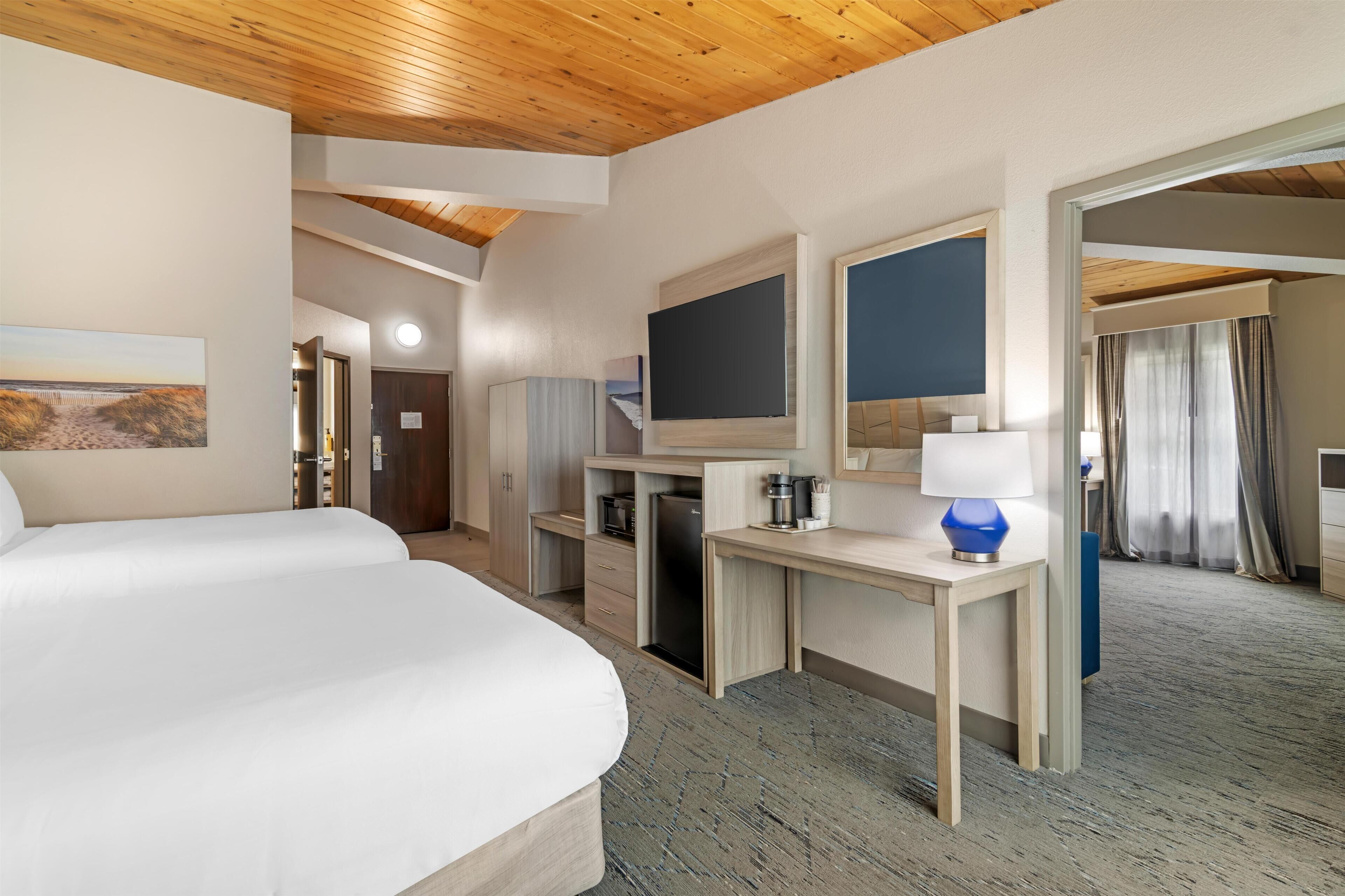 A hotel room with a large bed, a desk with a computer, a TV, and a small kitchenette.