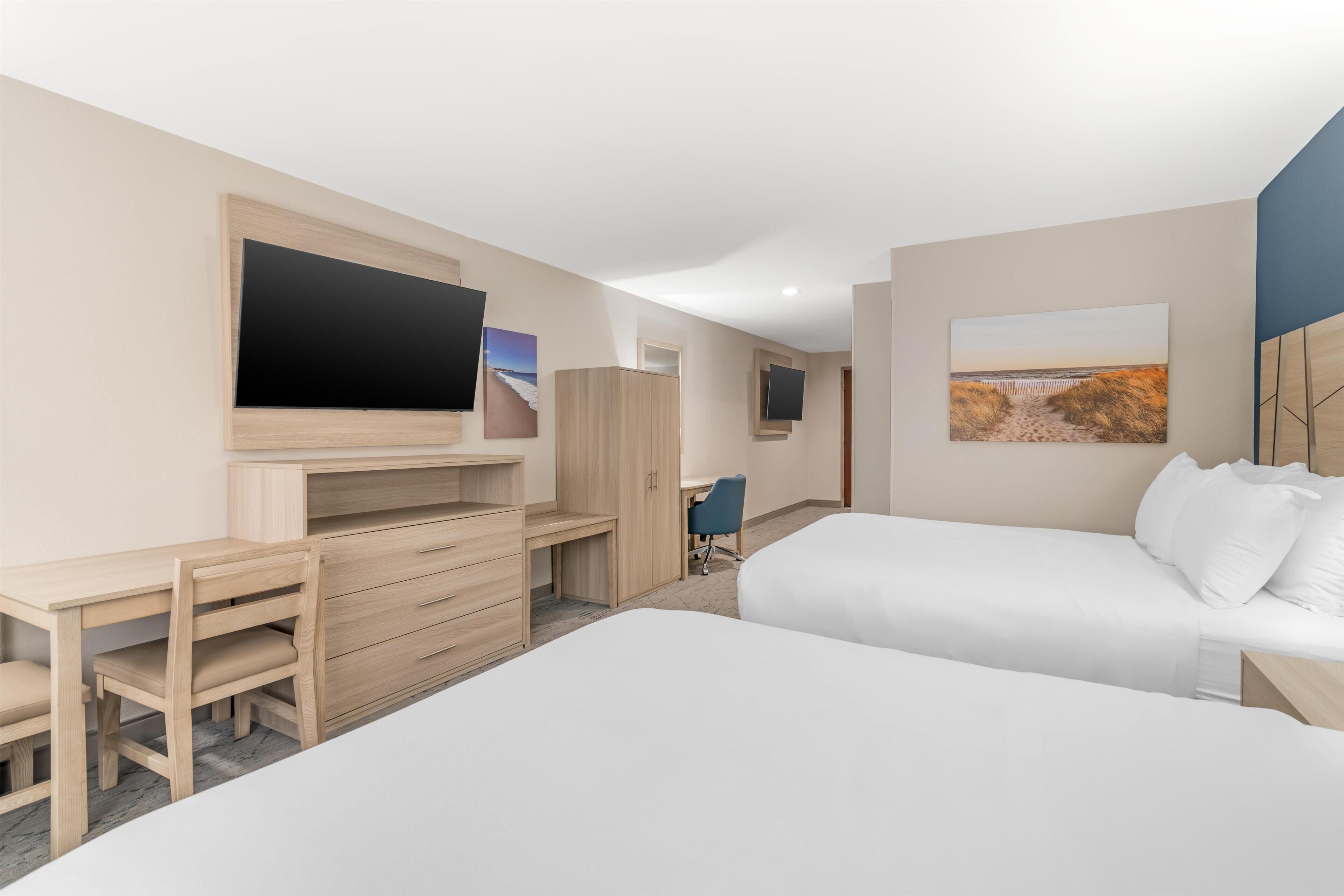 A hotel room with a bed, a desk with a chair, a TV, and artwork on the walls.