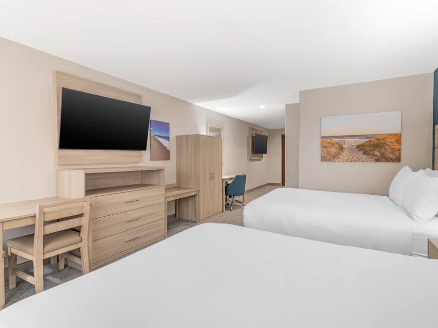 A hotel room with a bed, a desk with a chair, a TV, and artwork on the walls.