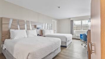 A hotel room with two beds, a desk, a chair, and a window with a view of a fence.