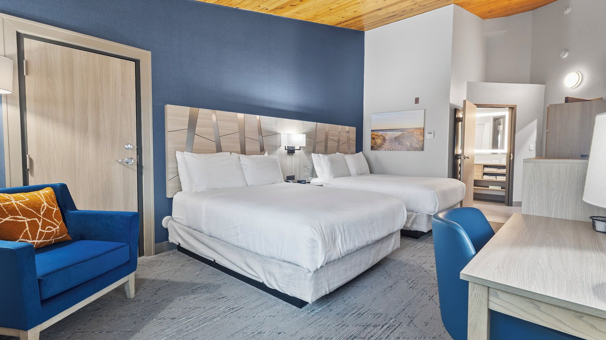 Habitación de hotel con dos camas, un escritorio, una silla y un armario.